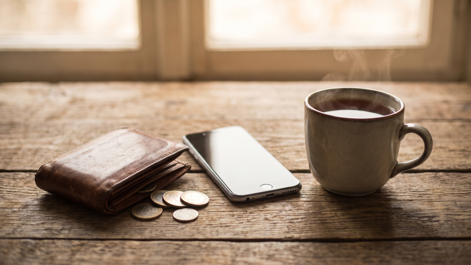 机の上のスマホと小銭入れ、お茶。料金を意識して使う注意点のイメージ
